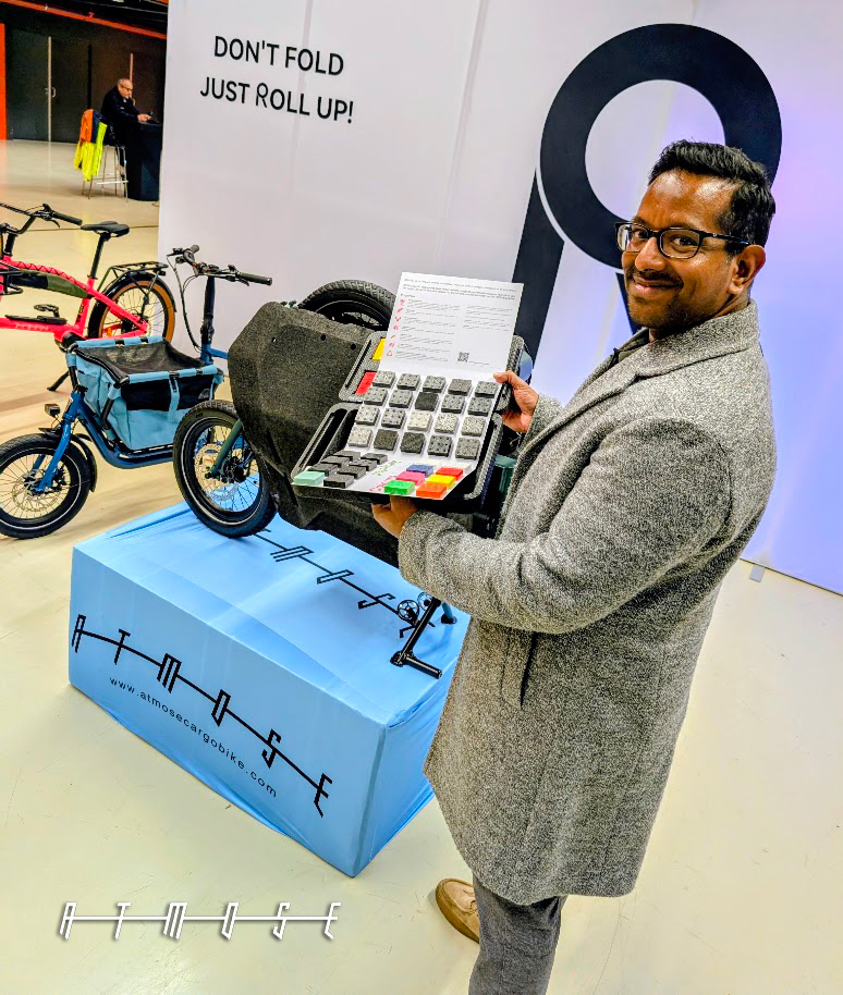 A visitor holding the ATMOSE colour sample board beside a folded cargo bike box on the stand
